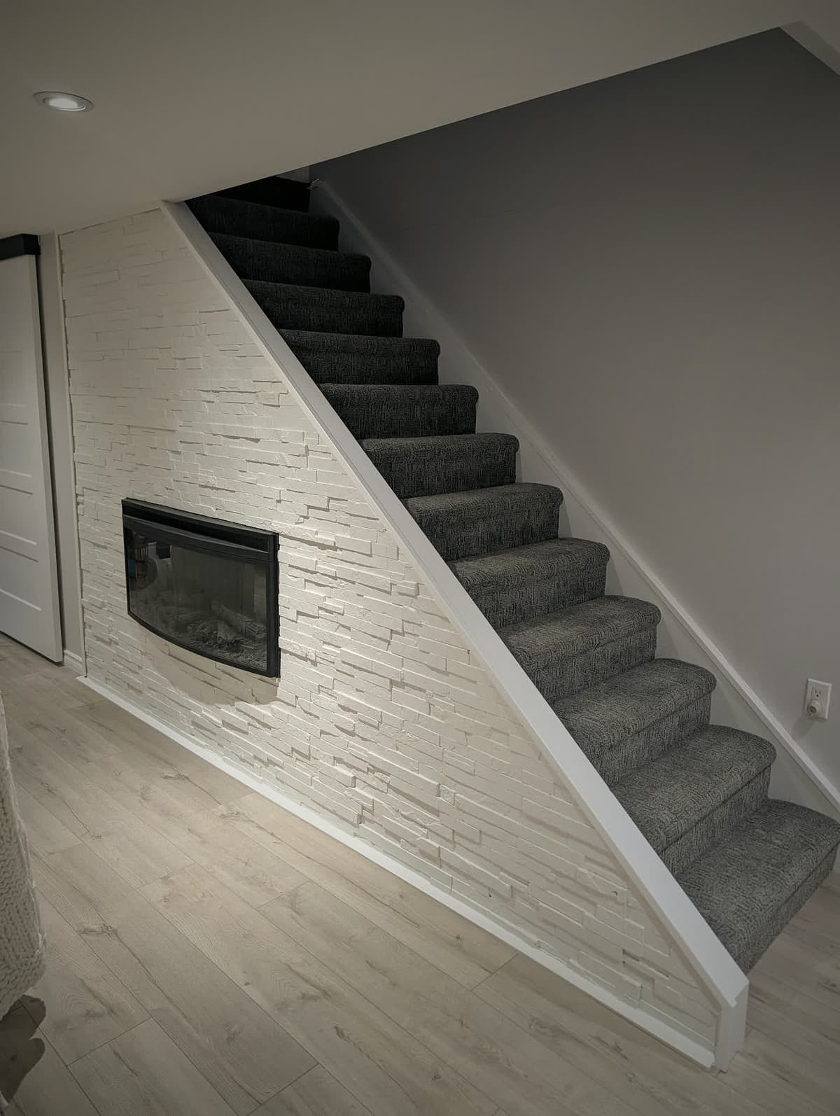 Finished basement with a stone feature wall, linear fireplace, and carpeted stairs