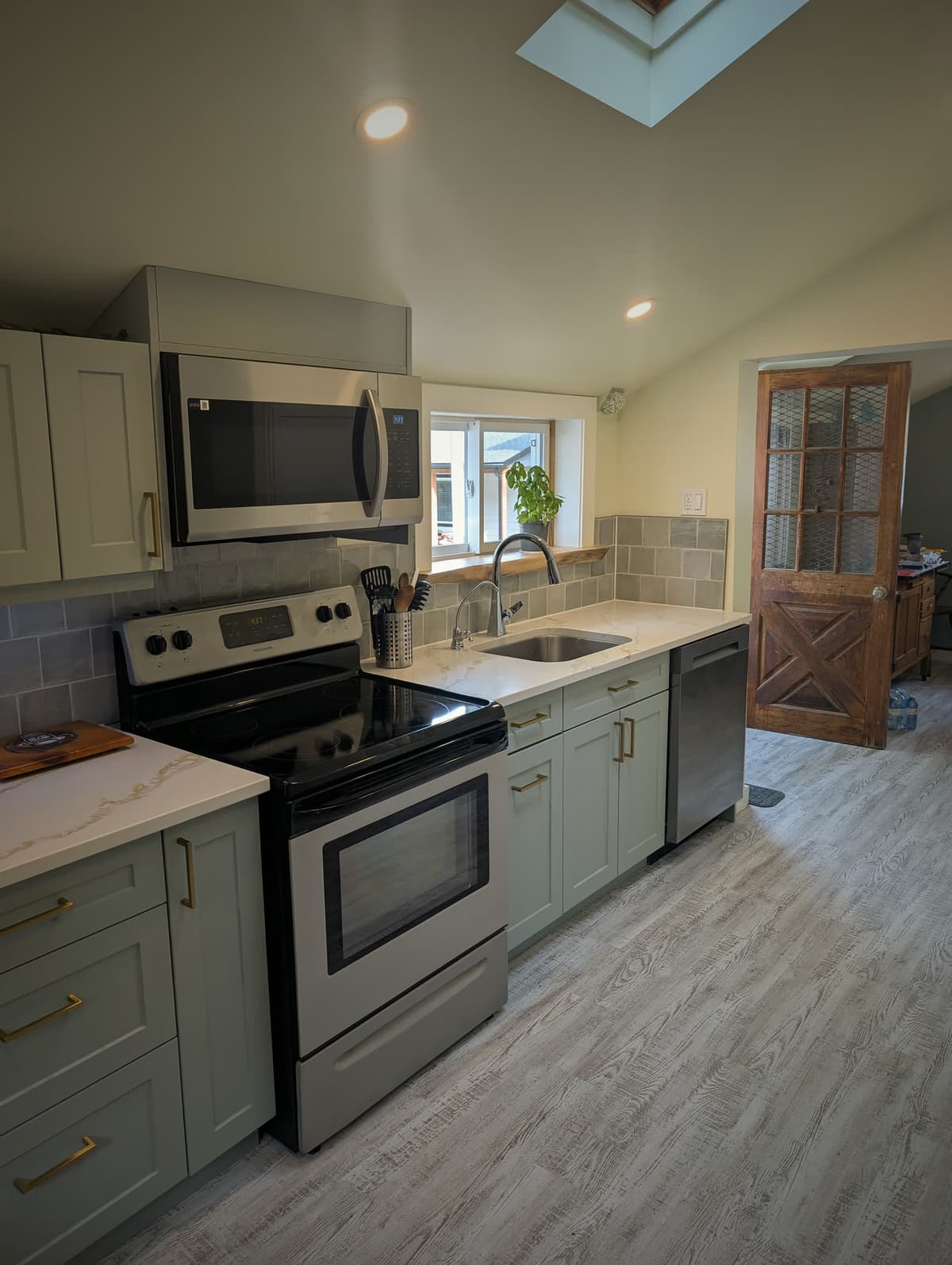 Finished kitchen with sage green shaker cabinets, brass hardware, and quartz counters